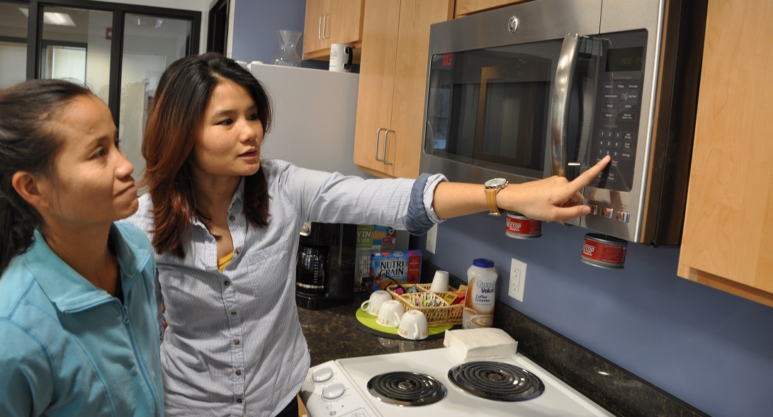 Worker teaching a refugee how to use a microwave.