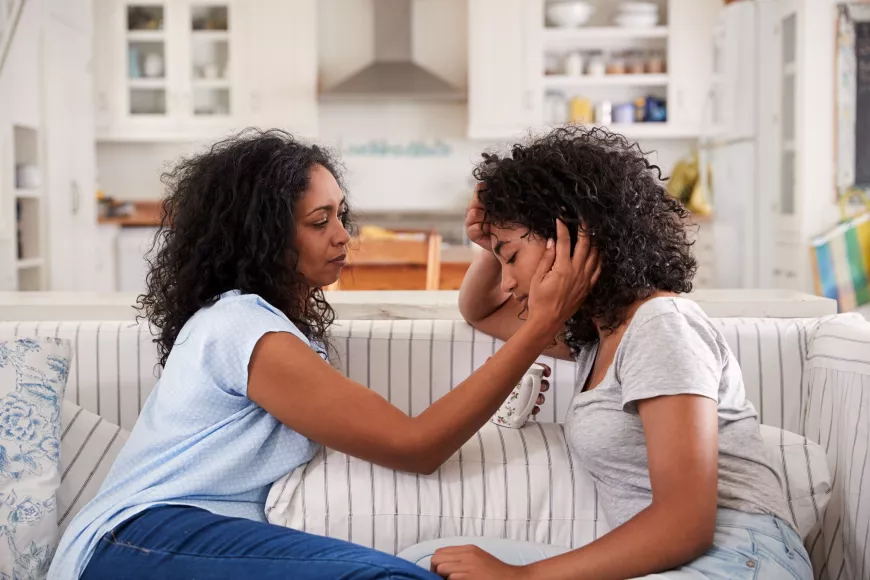 Mother comforts teen while sitting on a couch.