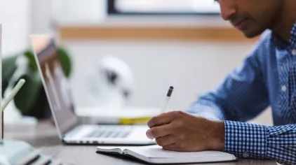 A person writing in a notebook, sitting at a desk