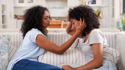 Mother comforts teen while sitting on a couch.